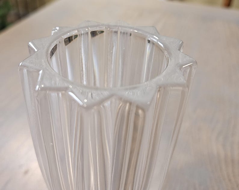 Pu&ograve; includere: Vaso di vetro trasparente con bordo a forma di stella. Il vaso presenta delle scanalature verticali e una forma svasata. Il bordo ha una serie di punte, che gli conferiscono un aspetto decorativo. Il vetro &egrave; trasparente.