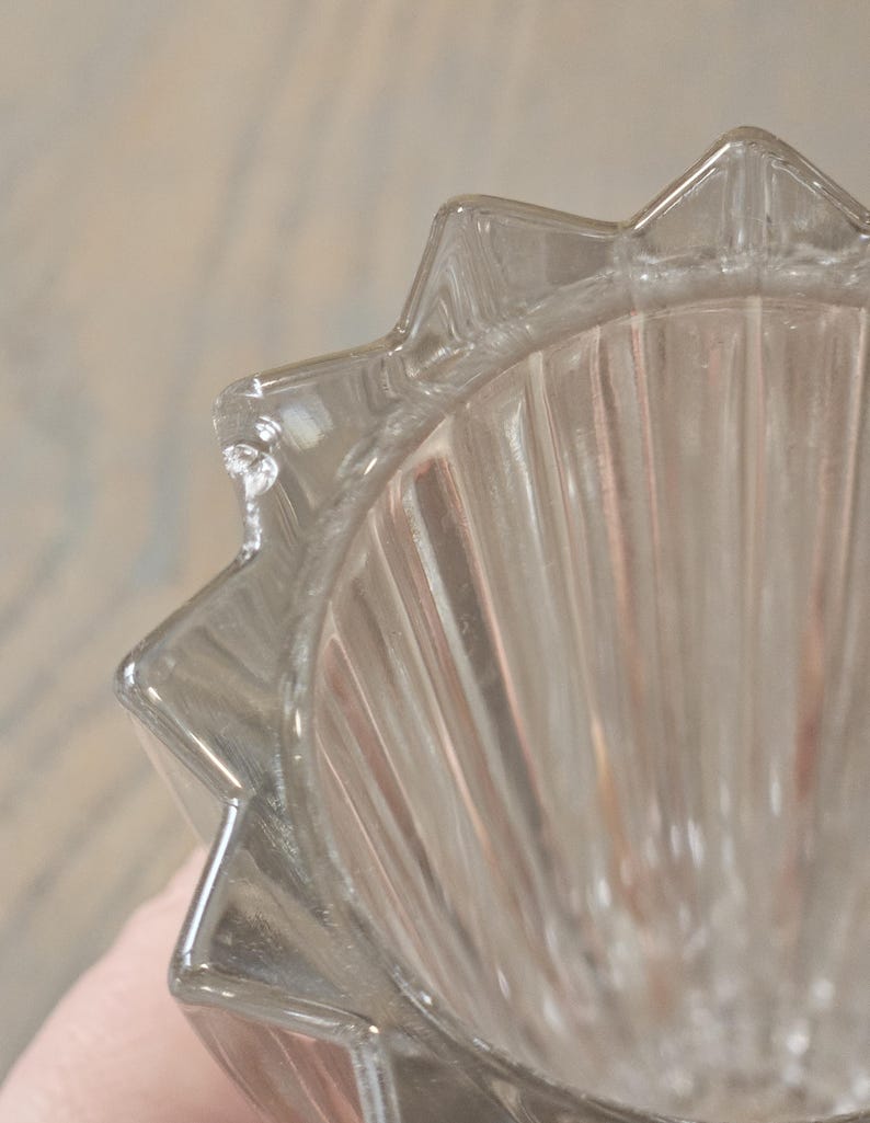 Pu&ograve; includere: Primo piano di una ciotola di vetro trasparente con bordo a stella. La ciotola presenta dettagli a coste verticali all'interno. Il vetro &egrave; trasparente, permettendo alla luce di passare, e i bordi sono ben definiti.