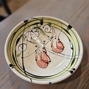 May include: A white ceramic bowl with a green, yellow, and black striped design. The bowl has a hand-painted design of pink flowers and leaves.