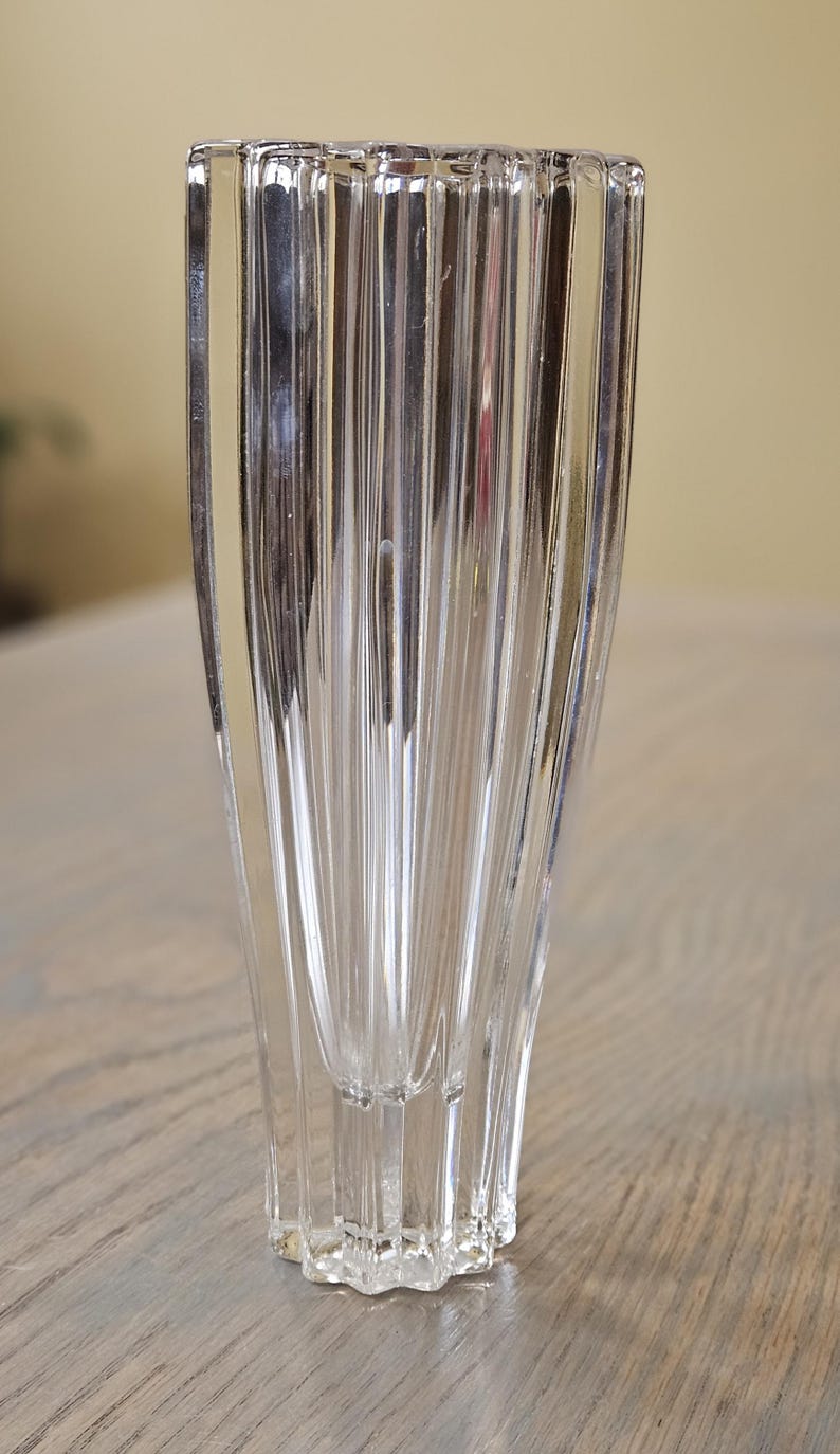 Pu&ograve; includere: Un vaso di vetro trasparente scanalato con un design geometrico unico. Il vaso ha una forma rettangolare con scanalature verticali, creando una superficie strutturata. La base ha una forma a stella. Il vaso &egrave; alto circa 15 cm.