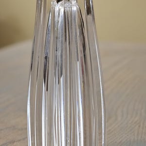 Pu&ograve; includere: Vaso di vetro trasparente con base a forma di stella e design a coste verticali. Il vaso ha una forma alta e sottile con una parte superiore svasata. Il vetro &egrave; trasparente, permettendo alla luce di passare, ed &egrave; posto su una superficie di legno.