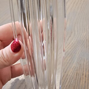 Pu&ograve; includere: Vaso di vetro trasparente con design a coste verticali. Il vaso ha una forma rettangolare con base svasata e parte superiore leggermente pi&ugrave; ampia. Il vaso &egrave; tenuto in mano con smalto rosso glitterato.