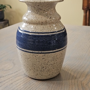 May include: A set of three ceramic mugs with a speckled, matte finish. The mugs are in shades of cream, light gray, and dark gray. Each mug has a simple, minimalist design and a rounded handle. The mugs are stacked on top of each other.