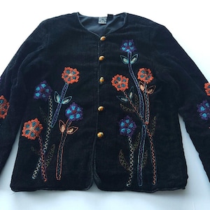 Pode incluir: Casaco de veludo cotelê preto com design floral bordado. O casaco apresenta flores laranja e azuis com folhas e caules verdes. Possui botões dourados e mangas compridas.