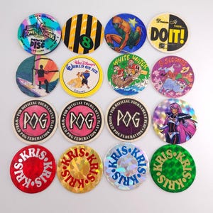 May include: A collection of sixteen circular cardboard game discs arranged in a four-by-four grid. The discs feature various colorful graphics, including Power Rangers, Disney characters, POG tournament logos, and holographic designs with the text KRIS.