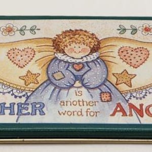 Pode incluir: Uma lata retangular de metal com borda verde escura apresentando uma ilustração central de um anjo com cabelos castanhos cacheados, vestido azul e grandes asas decoradas com corações e estrelas. O texto diz MOTHER is another word for ANGEL.