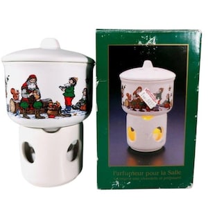 May include: A white ceramic potpourri warmer with a lid, featuring a colourful illustration of Santa Claus and forest animals. The base has circular cutouts for ventilation. It is displayed next to its original green box with product text.