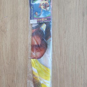 Könnte beinhalten: Power Rangers Diamant Drachen in einer transparenten Kunststoffverpackung. Der Drachen zeigt Bilder von Power Rangers-Charakteren und den Text "READY TO FLY". Der Drachen ist gelb, rot und blau.