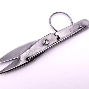 May include: Vintage metal scissors with a loop handle. The scissors have a silver finish and a pointed blade. The text "SCISSOR AIR PAT. 192" is visible on the handle. The scissors are on a white background.
