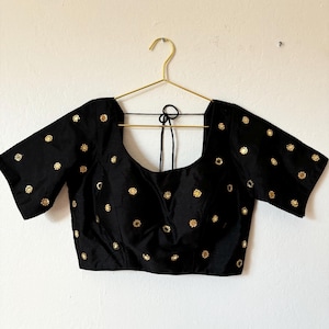 Puede incluir: Una blusa negra de manga corta con adornos de espejo dorado en un patrón floral.
