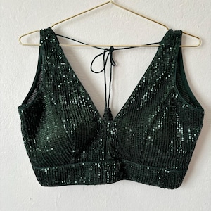 Puede incluir: Un top corto de lentejuelas verde oscuro con escote en V y un lazo en la espalda.