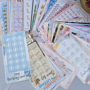 May include: A collection of colourful stickers with various designs, including hearts, lightning bolts, cars, and bees. The stickers are arranged in a fan shape and have a variety of text, including "£10 Savings", "TV License", "Gas and Electricity", and "Anniversary".