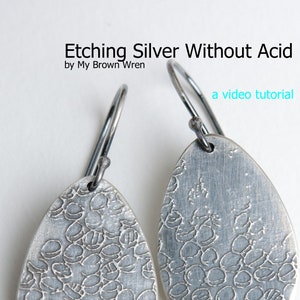 May include: A pair of silver earrings with a textured, patterned design. The earrings are shaped like teardrops and have a simple wire hook closure. The earrings are titled "Etching Silver Without Acid" and are described as a video tutorial.