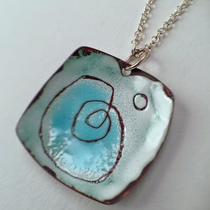 May include: A square pendant necklace with a blue and white enamel design. The pendant has a red border and a silver chain.