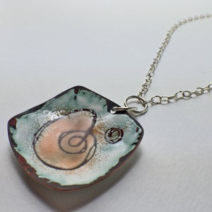 May include: A square pendant necklace with a silver chain. The pendant is made of copper and has a white, green, and pink enamel design. The design features a swirl pattern.