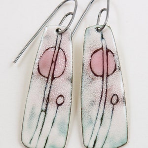 May include: A pair of dangle earrings with a white, pink, and green enamel design. The earrings have a silver hook closure.
