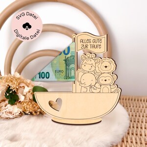 May include: Wooden sailboat money holder with a heart cutout and a banner that reads "Alles Gute zur Taufe". The sailboat is decorated with a giraffe, lion, elephant, and monkey.