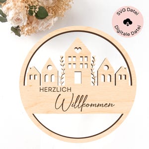 May include: A wooden round sign with a brown border and a cut-out design of houses with hearts and the text "Herzlich Willkommen".