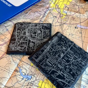May include: Two black slate coasters with a white graphic of an airport map. The map includes the text "GORE" and "PUEBLO RESERVOIR".