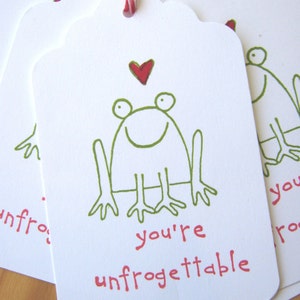 May include: A white gift tag with a green frog illustration and a red heart. The tag says "you're unfrogettable".
