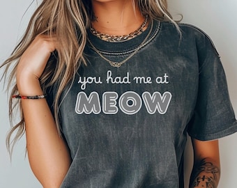May include: A black t-shirt with the text "you had me at MEOW" printed in white. The text is in a playful, bubble-like font.