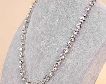 Può includere: Una collana d'argento con una fila di pietre di cristallo trasparenti.