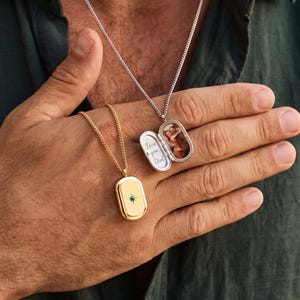 May include: Two oval locket necklaces on chains. One is gold-toned with a small green stone in the center. The other is silver-toned and open, revealing a photograph of two people and the engraved text "Love you Dad" inside the locket.