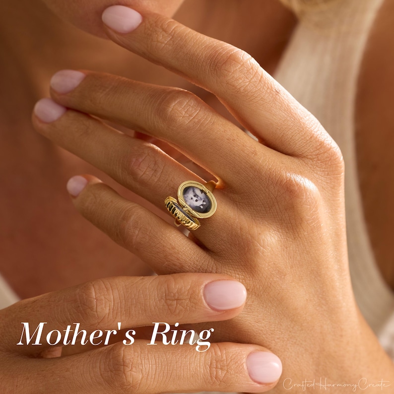 May include: A gold Mother's Ring with an oval locket containing a black and white image. The ring is open, revealing the image. The text "Mother's Ring" is displayed in white at the bottom of the image.