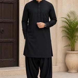 Puede incluir: Un kurta negro liso de manga larga con cuello mao y tapeta de botones, combinado con pantalones shalwar plisados y holgados a juego. El conjunto se completa con zapatos de cuero negro sin cordones y un reloj de pulsera oscuro.