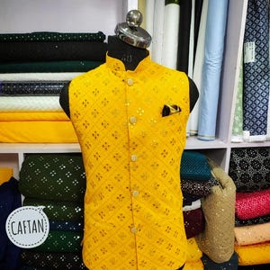 May include: A vibrant yellow waistcoat with a geometric design and gold detailing. It features a mandarin collar, button fastening, and a pocket square. The word "CAFTAN" is in a white circle. The waistcoat is displayed on a mannequin, size 40.