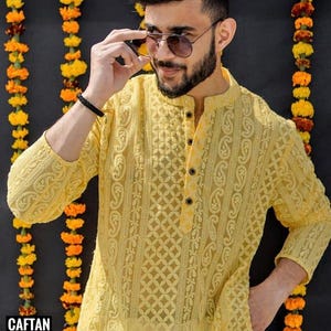 May include: A yellow embroidered kurta with a button-up collar and long sleeves. The kurta is made of a sheer fabric and has a delicate floral pattern. The model is wearing sunglasses and has a beard.