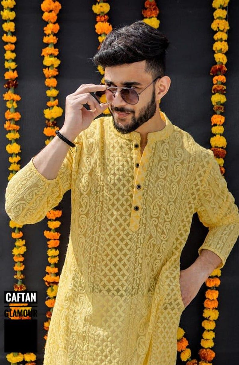 May include: A yellow embroidered kurta with a button-up collar and long sleeves. The kurta is made of a sheer fabric and has a delicate floral pattern. The model is wearing sunglasses and has a beard.