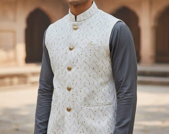 May include: A cream-colored, patterned vest with gold buttons and a mandarin collar. The vest is worn over a gray long-sleeved shirt and matching pants. The outfit is suitable for formal occasions.