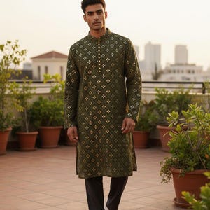 May include: An olive green kurta with a geometric gold pattern and a mandarin collar. The long-sleeved tunic is paired with black pants and white sneakers. The man is standing on a tiled patio with potted plants.