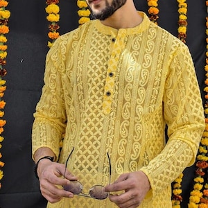May include: A yellow long-sleeved shirt with a button-up collar and intricate embroidery. The shirt has a paisley pattern and a geometric design.