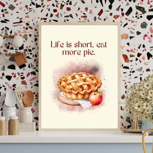 Può includere: Un design di arte murale stampabile con un'illustrazione ad acquerello di una torta di mele e una mela. Il testo "Life is short, eat more pie." è scritto in rosso.