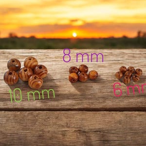 以下が含まれることがあります： 3つのサイズの木製ビーズ：10 mm、8 mm、6 mm。ビーズは茶色でストライプ模様です。画像は、背景に夕焼けのある木製の表面で撮影されています。