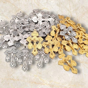 Puede incluir: Una colección de dijes religiosos de metal plateado y dorado en forma de cruces con grabados detallados. Los dijes están dispuestos en una pila, con los dijes dorados encima de los dijes plateados.