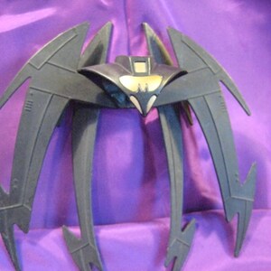 May include: Black plastic Batman wings with a yellow bat symbol on the front. The wings are designed to look like a bat in flight.