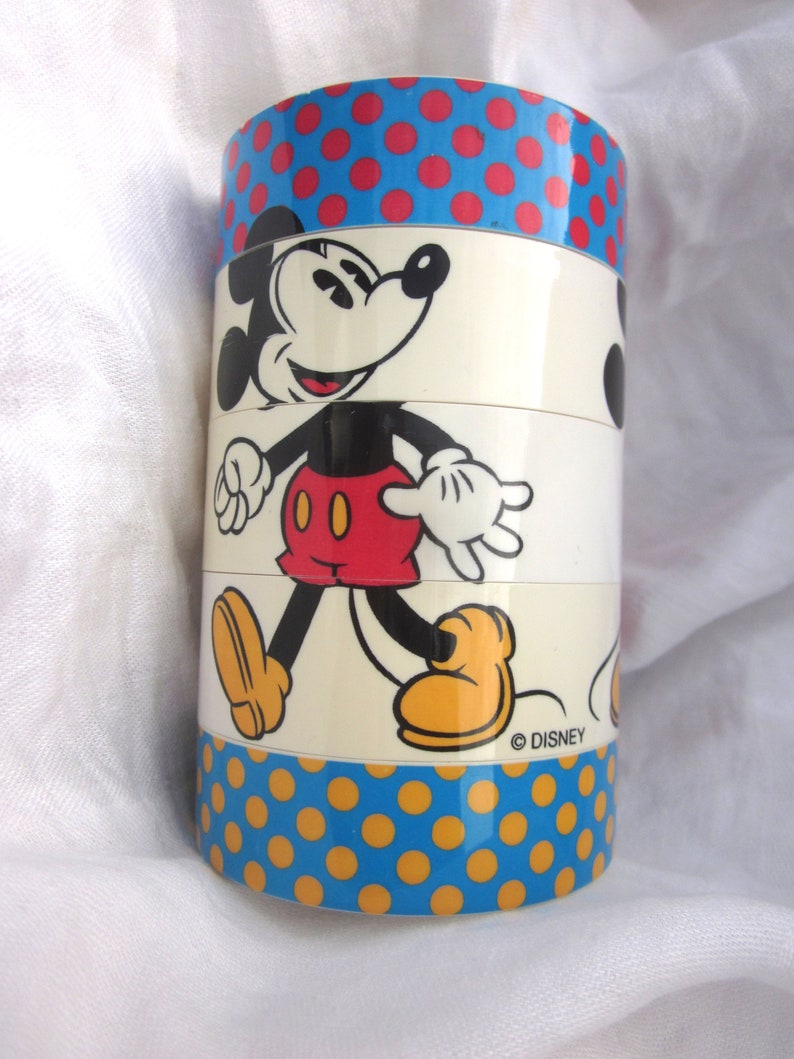 May include: A vintage stacking toy featuring Mickey Mouse. The toy is made of plastic and has a white background with a red, blue, and yellow polka dot pattern. The toy is labeled with the copyright symbol and the word "DISNEY".
