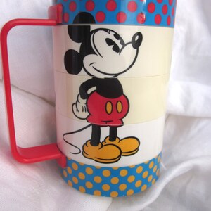 May include: A vintage Mickey Mouse stacking cup with a blue and red polka dot pattern. The cup features a cartoon image of Mickey Mouse in red shorts and yellow shoes.