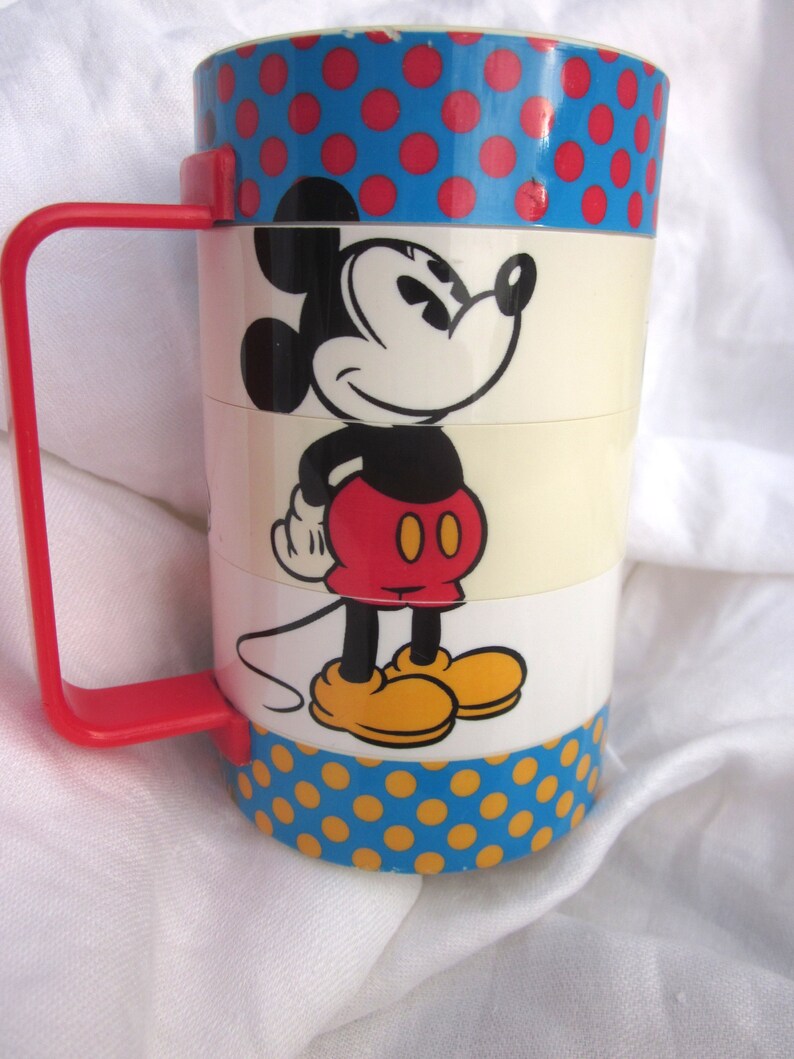 May include: A vintage Mickey Mouse stacking cup with a blue and red polka dot pattern. The cup features a cartoon image of Mickey Mouse in red shorts and yellow shoes.