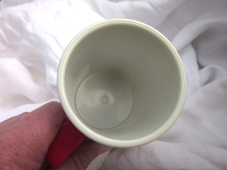 May include: A white ceramic mug with a red handle. The mug is empty and the inside is visible.