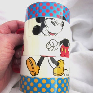 May include: A vintage Mickey Mouse stacking cup with a blue and yellow polka dot pattern. The cup features a red handle and a white background with a cartoon image of Mickey Mouse walking. The bottom of the cup has the text "&copy; DISNEY".