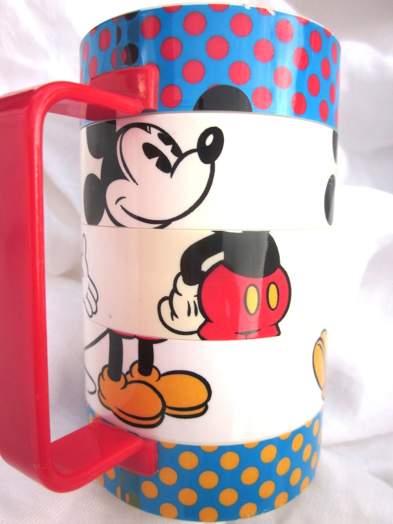 May include: A red and white ceramic mug with a blue and yellow polka dot pattern. The mug features a stacked design with multiple images of Mickey Mouse in different poses.