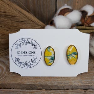 May include: A pair of oval-shaped earrings with a yellow, white, and blue marbled design. The earrings are set in gold-toned metal.