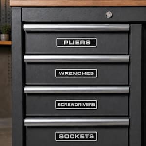 May include: A dark gray metal tool chest featuring four drawers with silver handles. Each drawer has a rectangular black and white label reading PLIERS, WRENCHES, SCREWDRIVERS, and SOCKETS from top to bottom. A silver key lock is visible at the top.