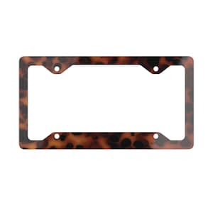 May include: A rectangular license plate frame with a tortoiseshell pattern. The frame has rounded corners and four mounting holes. The pattern features a mix of brown and black spots.