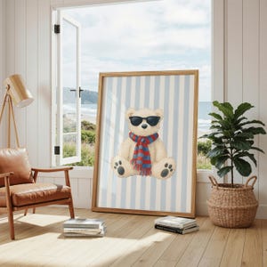 Könnte beinhalten: Ein gerahmter Druck mit einer Aquarellillustration eines Teddybären mit Sonnenbrille und einem rot-blau karierten Schal. Der Bär ist vor einem Hintergrund aus blau-weißen vertikalen Streifen platziert. Der Rahmen ist hellbraun.