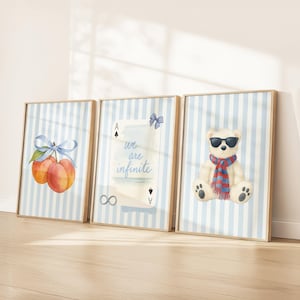 May include: Three framed art prints. The first features watercolor peaches with a blue bow. The second has the text "we are infinite" on a playing card. The third shows a teddy bear wearing sunglasses and a scarf. All are on blue striped backgrounds.
